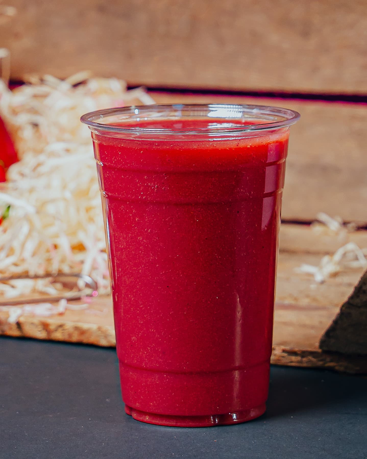 A clear cup of deep purple Açaí Kick smoothie against a dark studio background.
