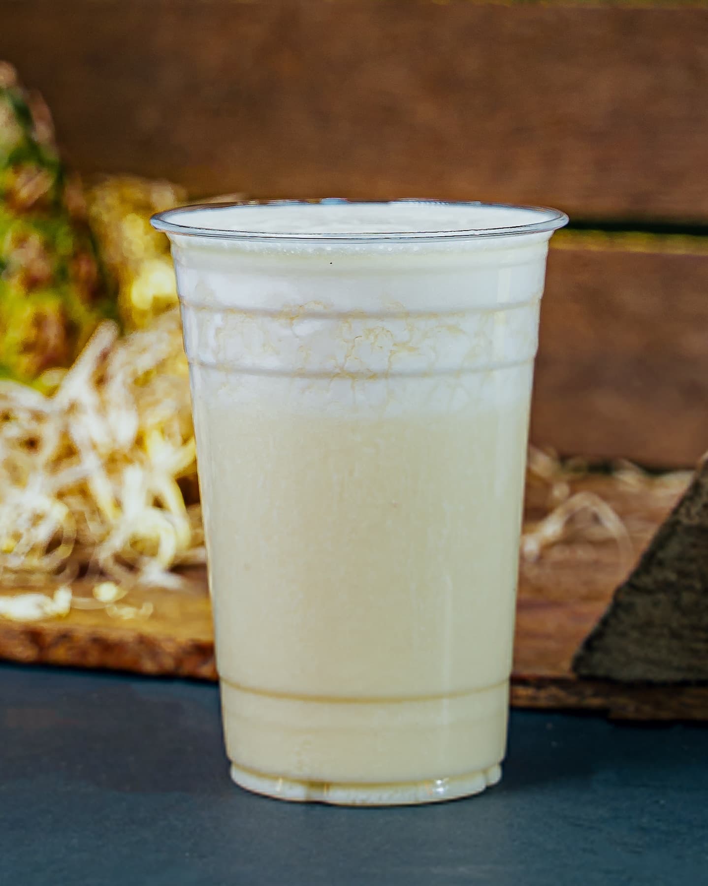 A clear cup of creamy pale Coconut Crush smoothie on a wood-plank studio backdrop.