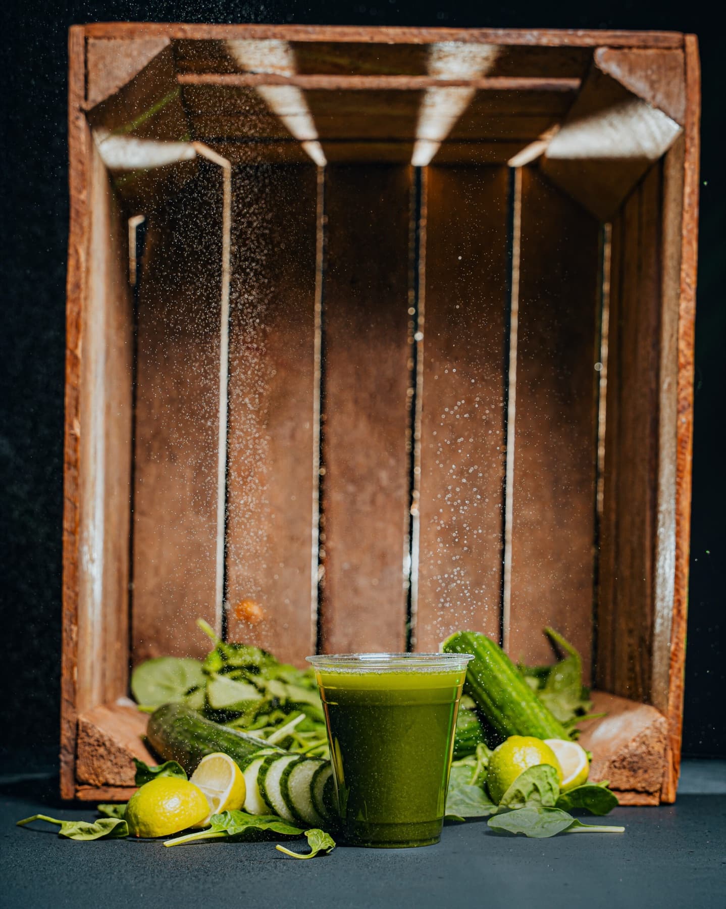 A clear cup of deep green Green Detox juice set inside a rustic wooden crate.