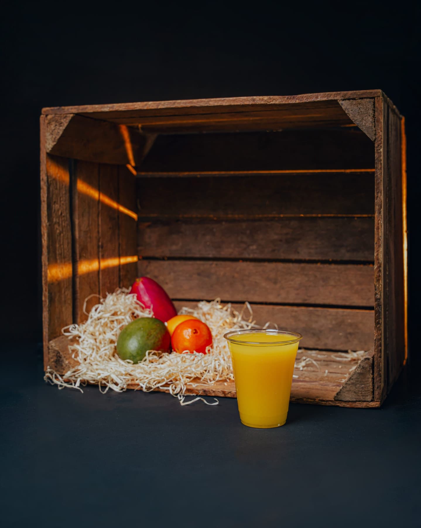 A clear cup of bright orange mango and orange juice on a studio set.