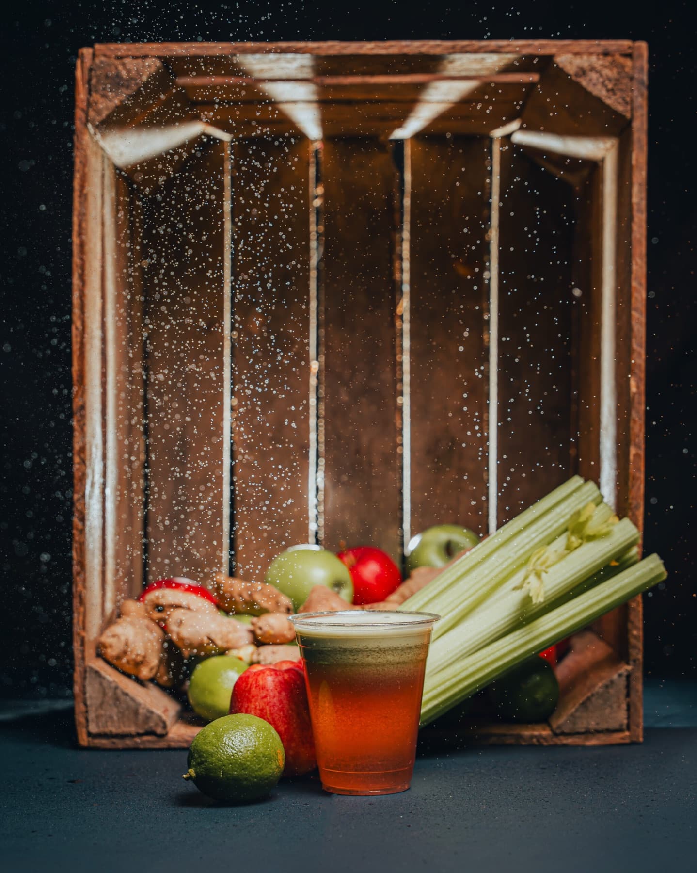 A clear cup of Mr Guts juice on a dark wooden studio backdrop.