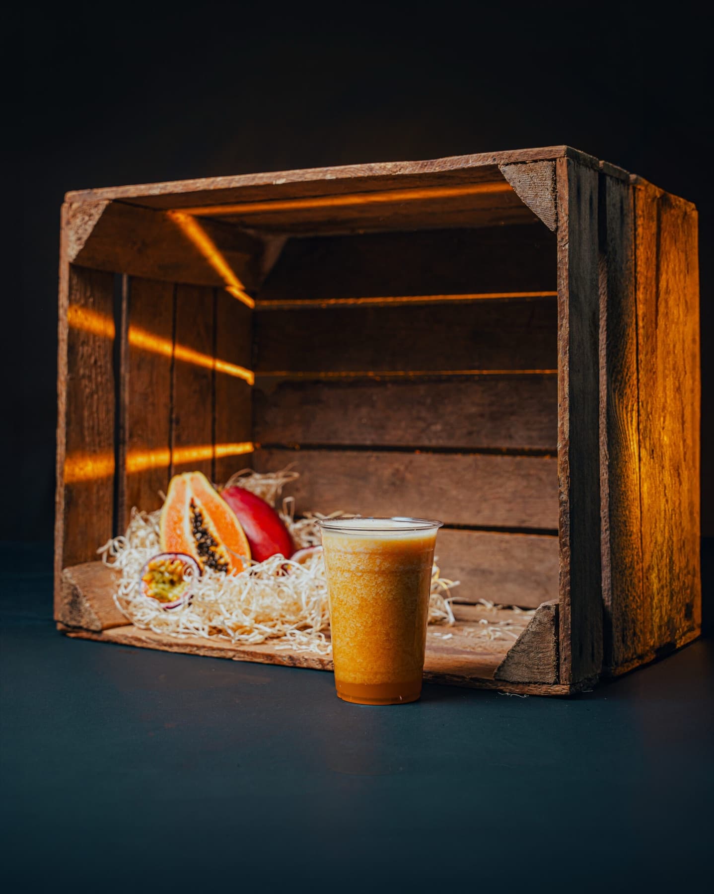 A clear cup of golden Passion Storm smoothie on a charcoal-and-wood studio set.