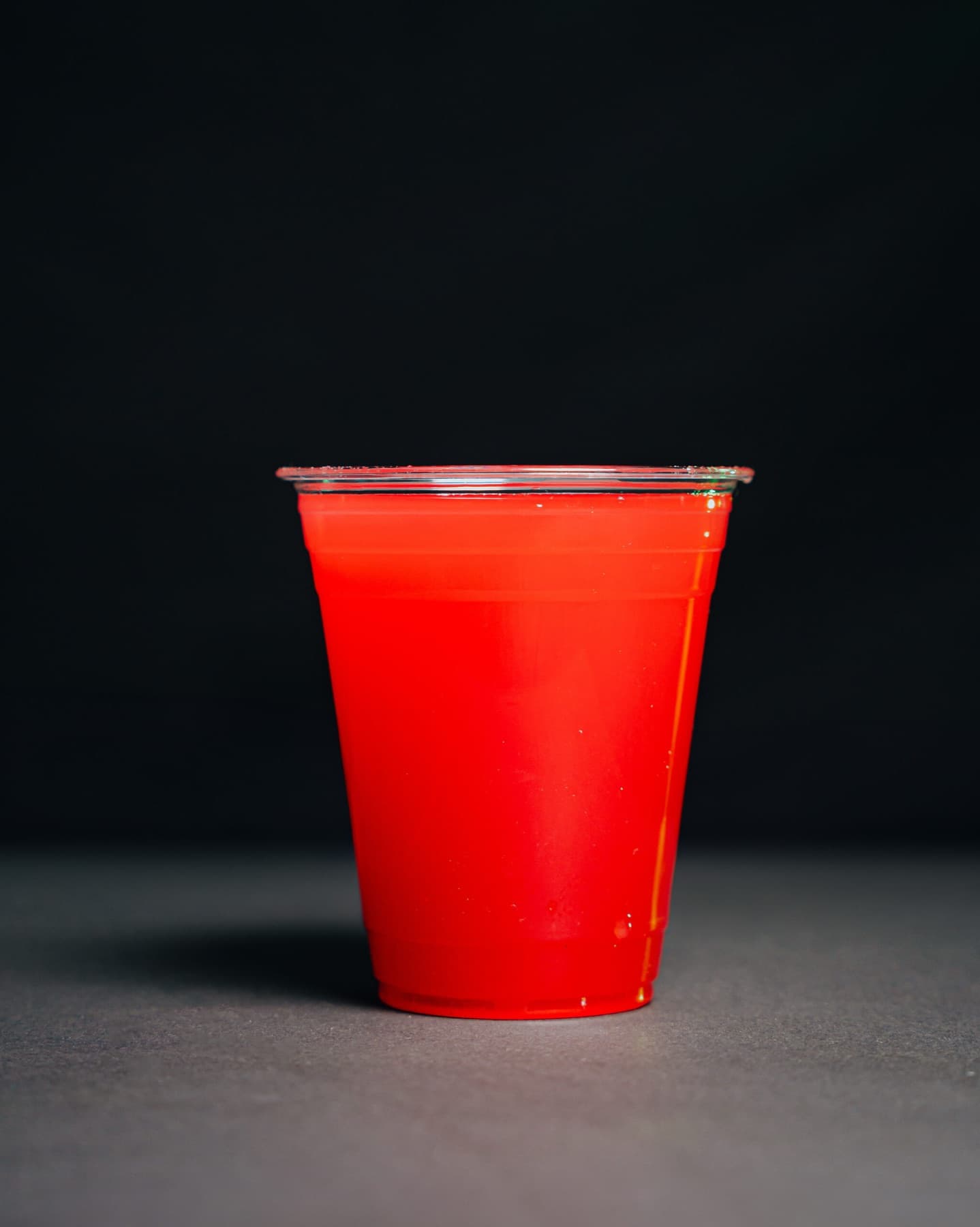 A clear cup of pink watermelon juice on a charcoal-and-wood studio set.