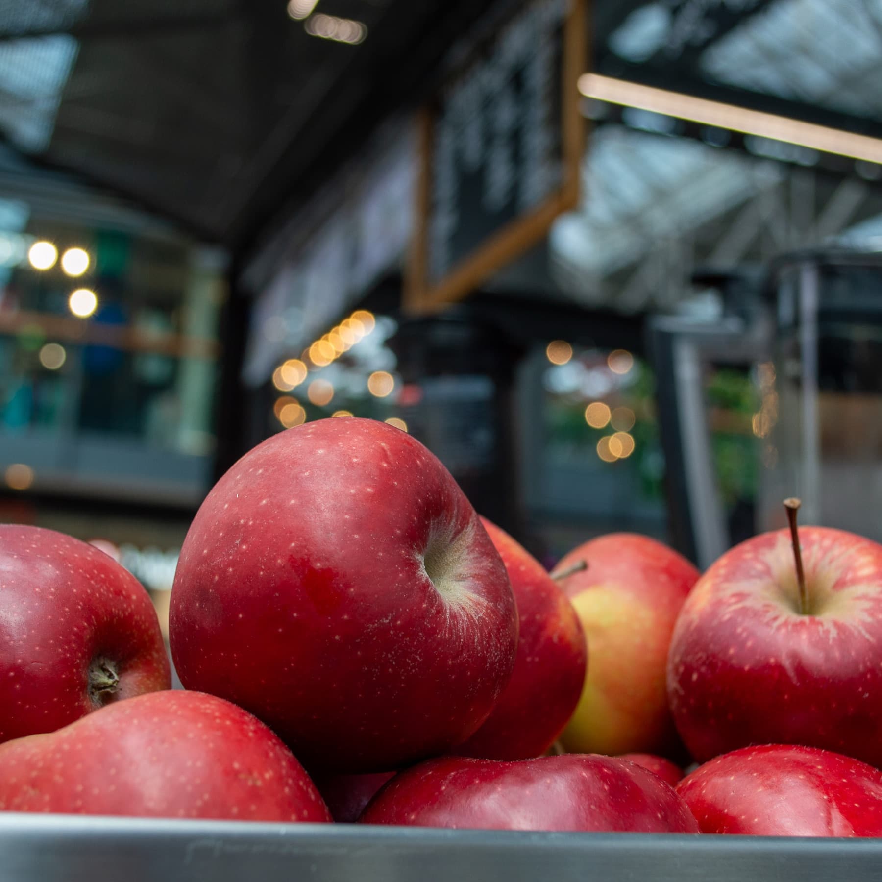 Fresh red apples in a tray at the market stall, the bustling market softly blurred behind.