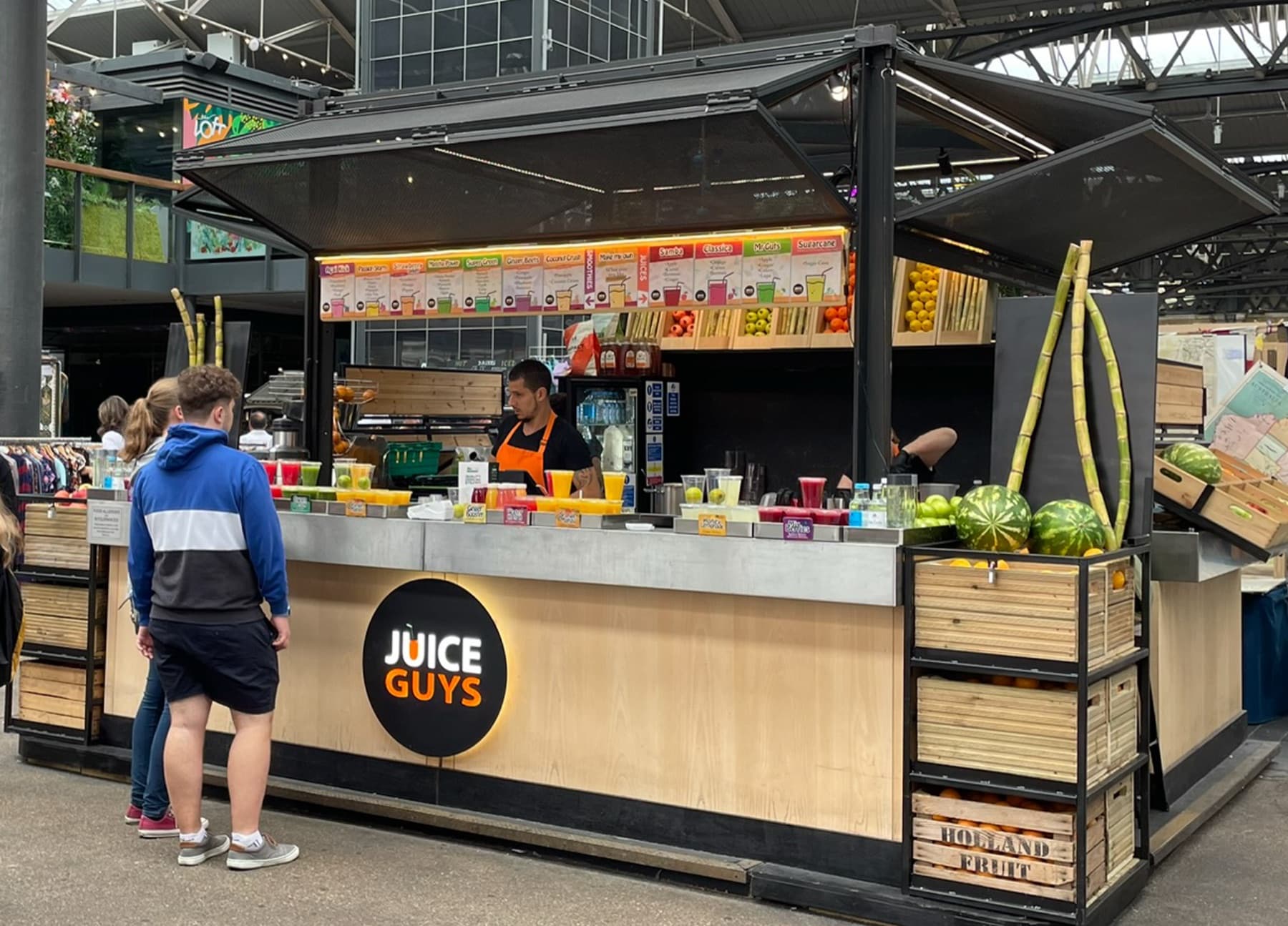 The Juice Guys stall at Old Spitalfields Market, with its round black badge sign, fresh produce and the team at work.